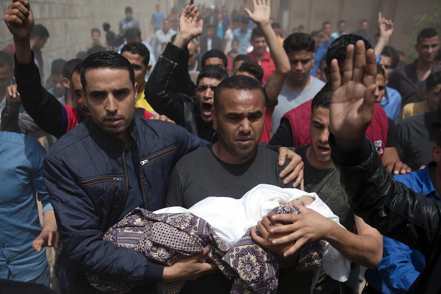 A dead child wrapped in white and a purple patterned scarf is carried by her three of her male relatives.