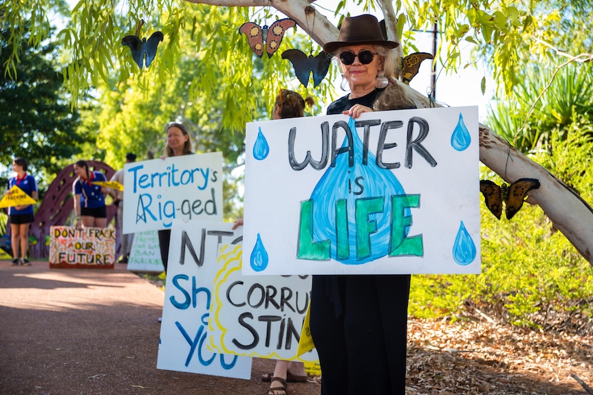 Una mujer está al frente de los manifestantes sosteniendo un cartel que dice que el agua es vida. 