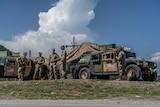 A group of soldiers dressed in army fatigues stand beside an army car on a base.