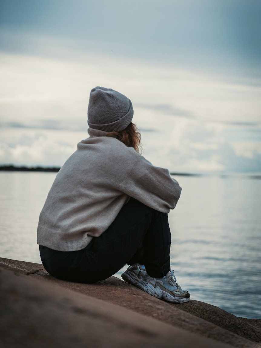 A woman sitting alone on a rock looking out to sea.