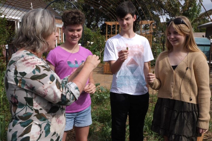 Three teenage children and a mother standing in the garden holding a leaf in their hand about to try them. 