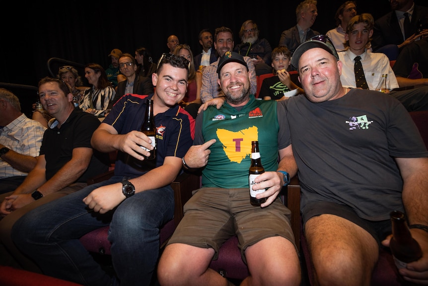 A man wears a traditional Tasmanian football guernsey surrounded by friends.