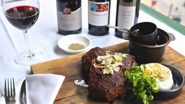 A table setting featuring a cut of meat and red wine.