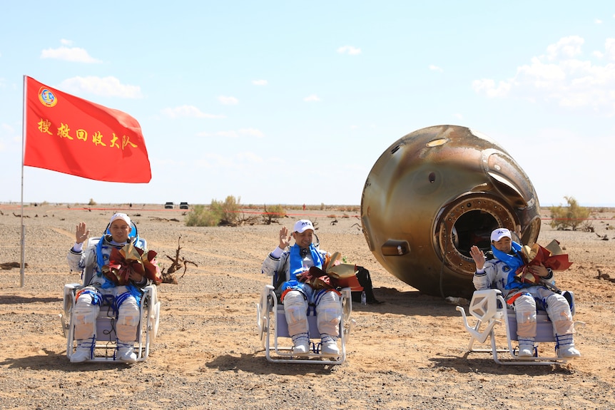 Trzech astronautów siedzi na półleżących ławkach na pustyni po wylądowaniu z misji.