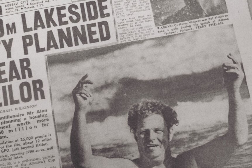 A man walks out of the water with his arms in the air, in a newspaper story