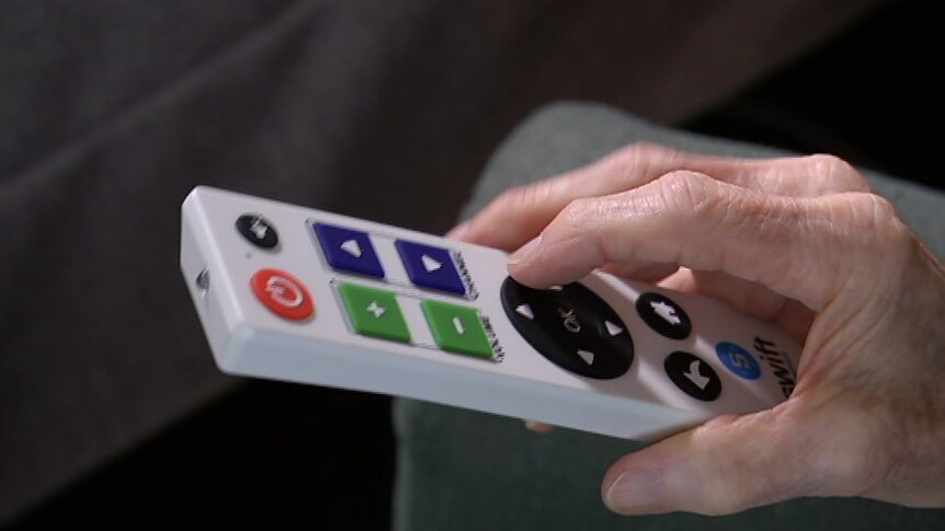 An elderly man using a large, white remote control