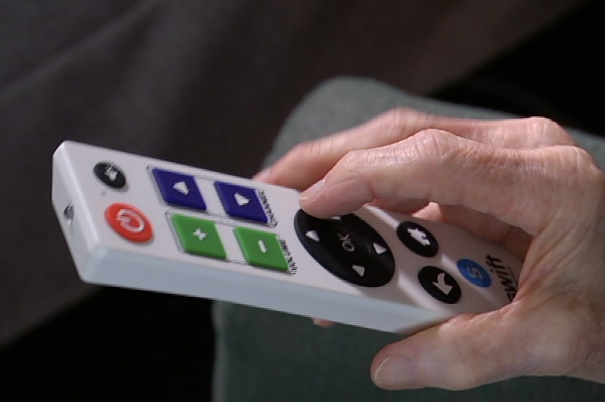 An elderly man using a large, white remote control