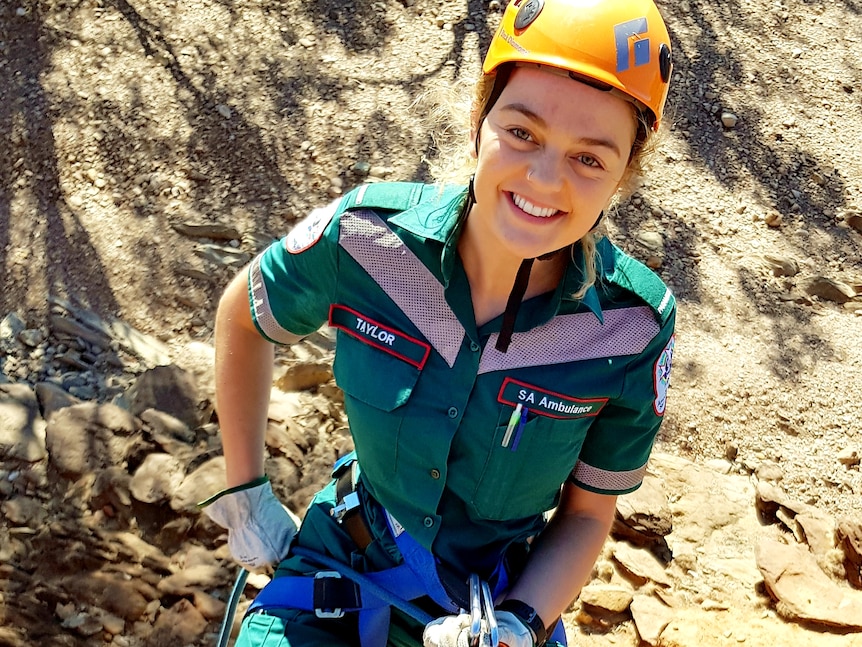 A woman wearing a green ambulance uniform and a helmet climbing up a rock cliff. 