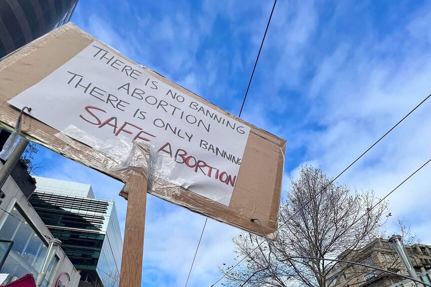 Two signs protesting anti-abortion laws are held aloft against a blue sky.