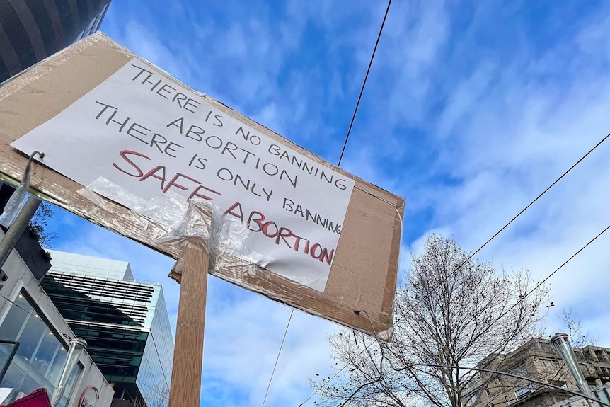 Two signs protesting anti-abortion laws are held aloft against a blue sky.