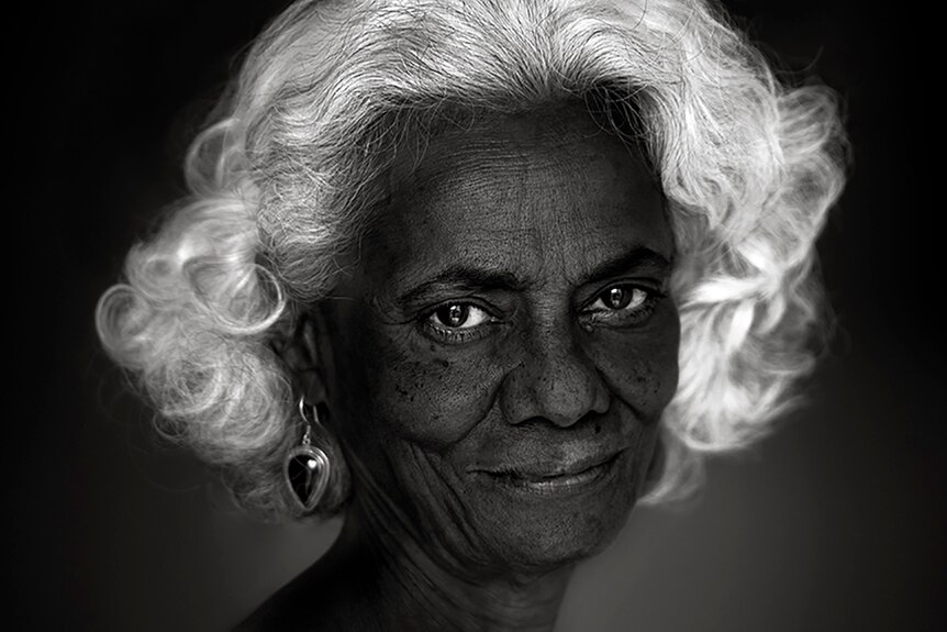 Black and white photo of woman with white hair, earrings, smiling.
