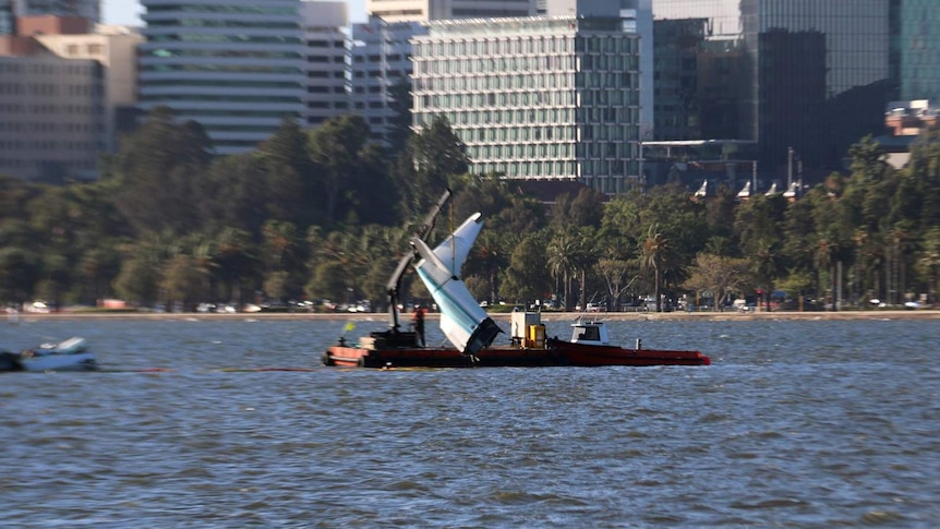 The torn-off tail of a sea plane is lifted from the Swan River by a crane on a barge.