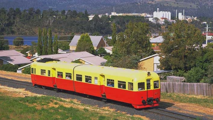 A red and yellow passenger train drives through Claremont.