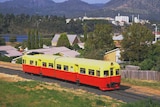 A red and yellow passenger train drives through Claremont.