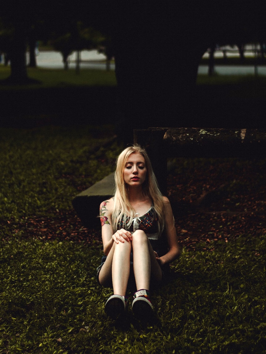 A young woman sits on the ground, meditating.