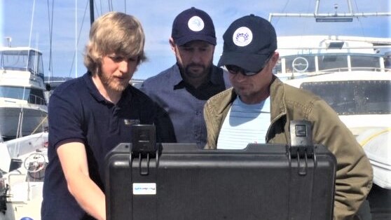 Kelsey Treloar with Dr Glenn Johnstone and Dr Jonny Stark looking at a drone controller unit.