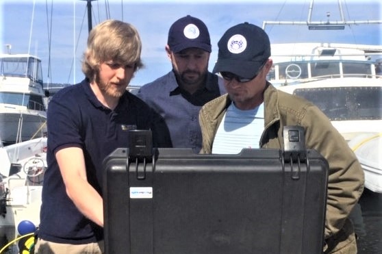 Kelsey Treloar with Dr Glenn Johnstone and Dr Jonny Stark looking at a drone controller unit.