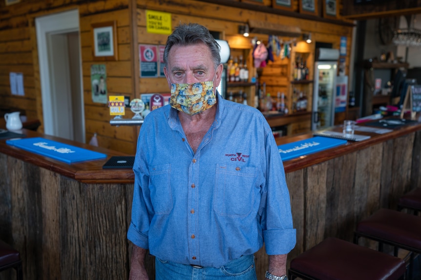 Un homme portant un masque facial covid regarde la caméra devant un bar.