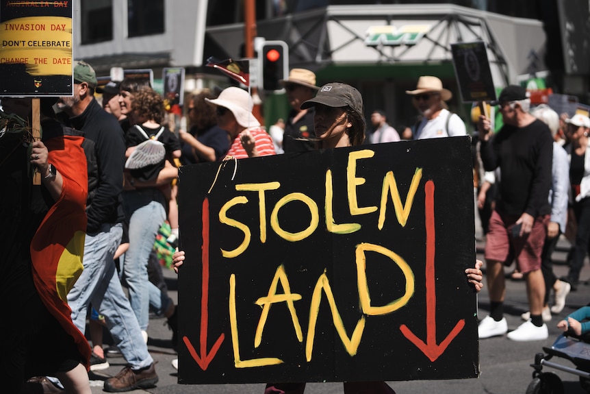 A woman holding a sign that says stolen land in the middle of a crowd of protesters. 