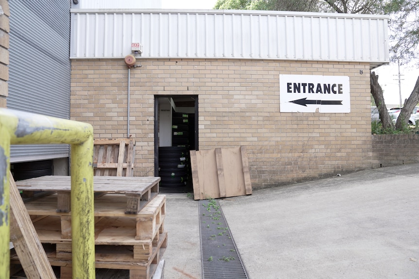 A warehouse, with brick walls, a large roller door, pallets and a sign saying 'entrance'