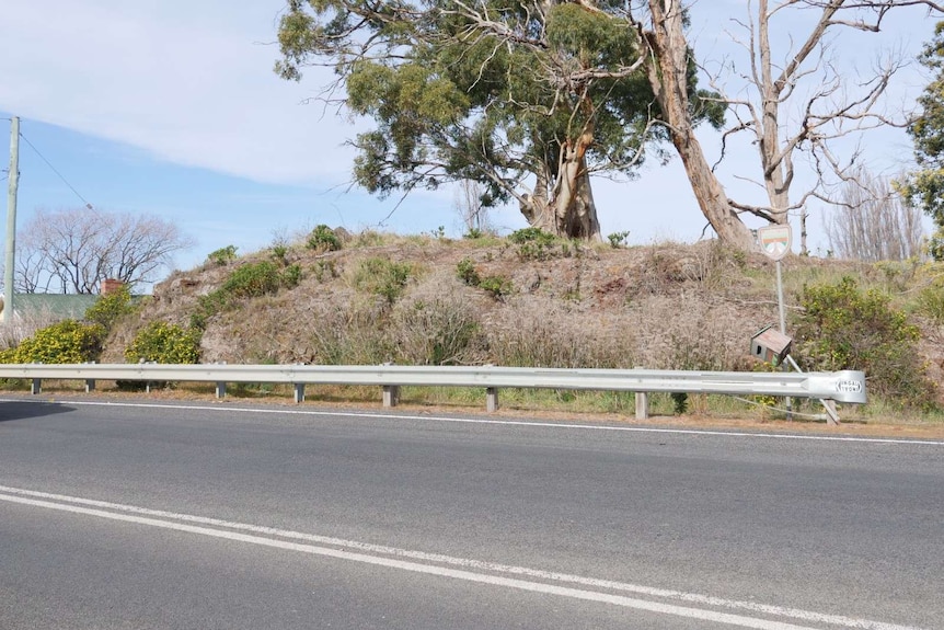 Photo of a road with a large rock with trees on top on the side