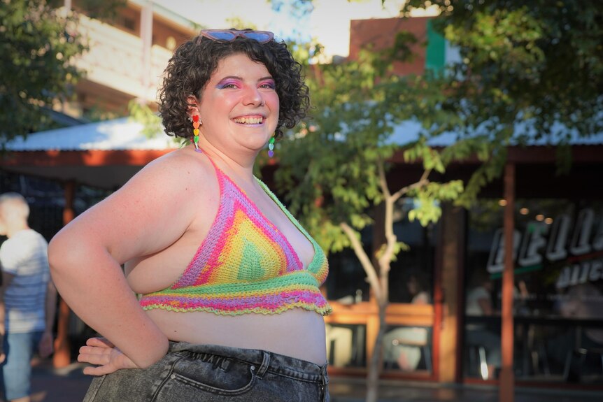 A girl in a crocheted rainbow top smiles at the camera