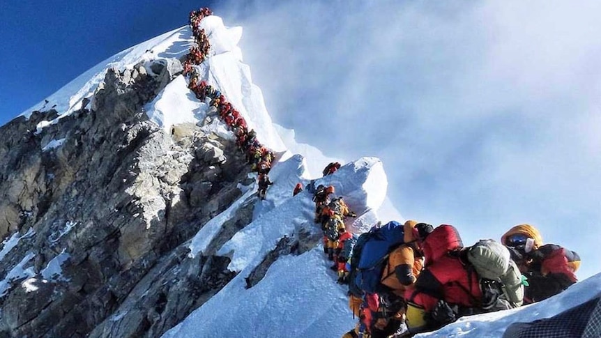 A line of climbers sit on the last ridge at the peak of a snow covered mount Everest.