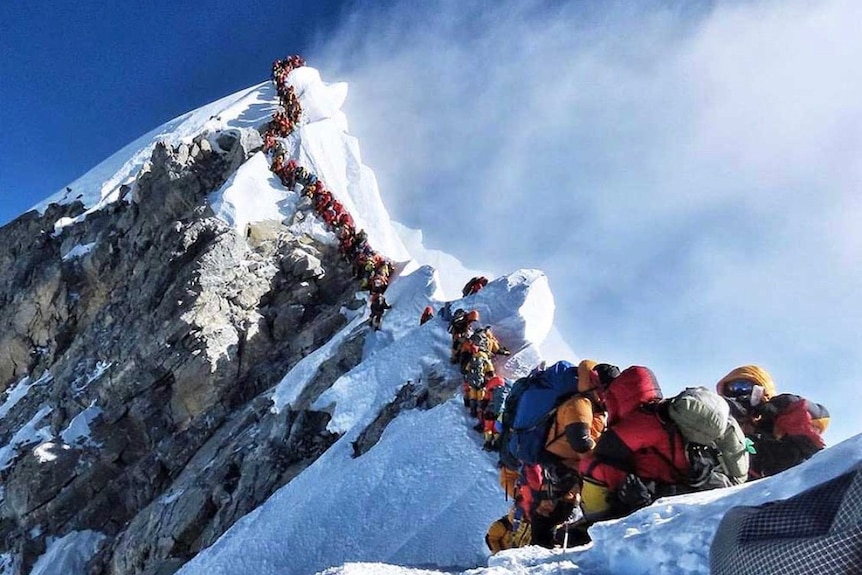 A line of climbers sit on the last ridge at the peak of a snow covered mount Everest.