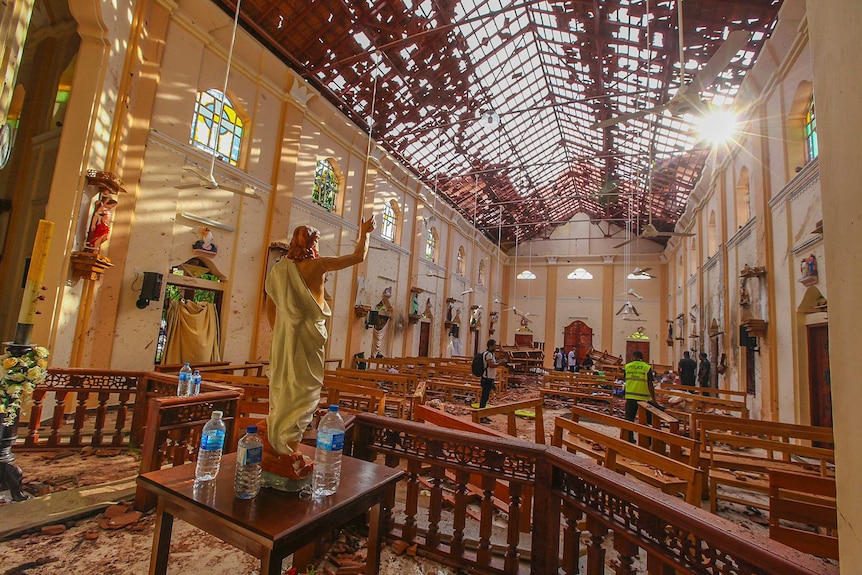 A church with a Jesus statue and sunlight coming through the bomb-damaged roof.