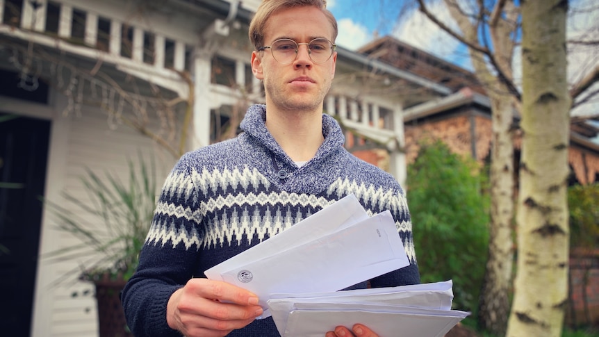 Man holds letter outside the front of his house.