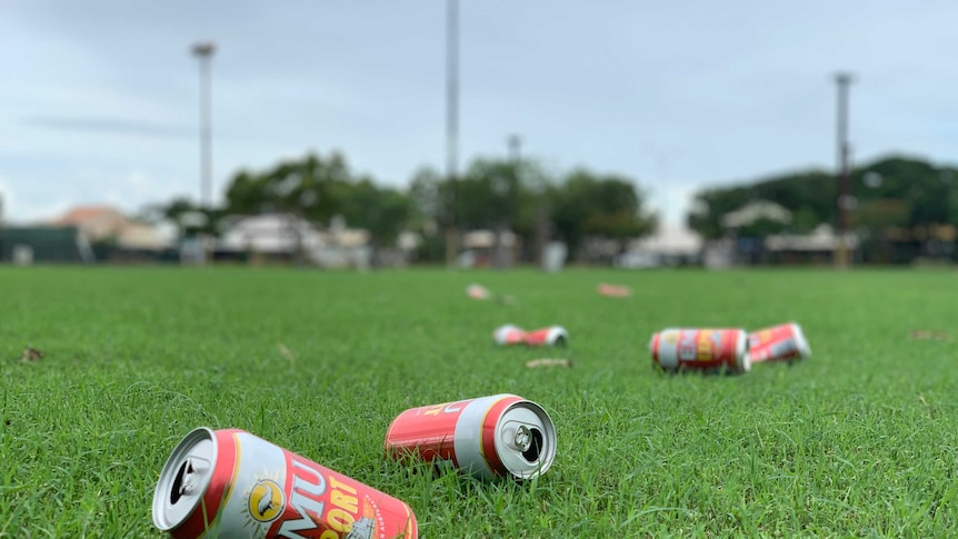 Cans of beer scattered across a green grassy field.
