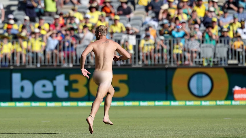 A streaker wearing no clothes runs on the playing surface at Perth Stadium in front of a crowd in the stands.
