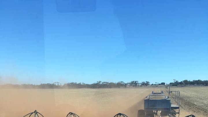 Tractor pulling along machinery planting seeds in a dry and dusty crop