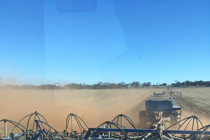 Tractor pulling along machinery planting seeds in a dry and dusty crop