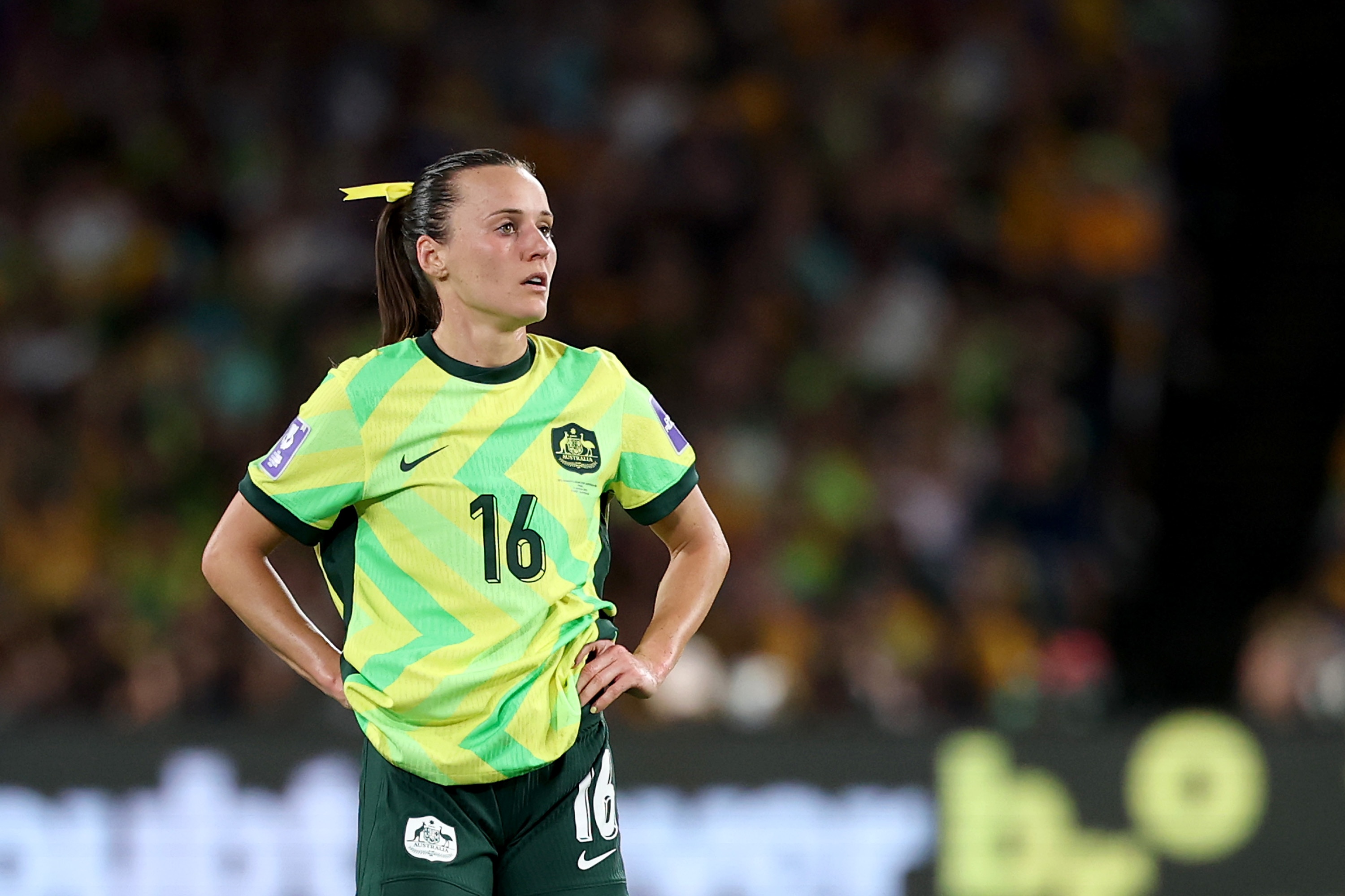 A soccer player in green and gold stands with hands on her hips