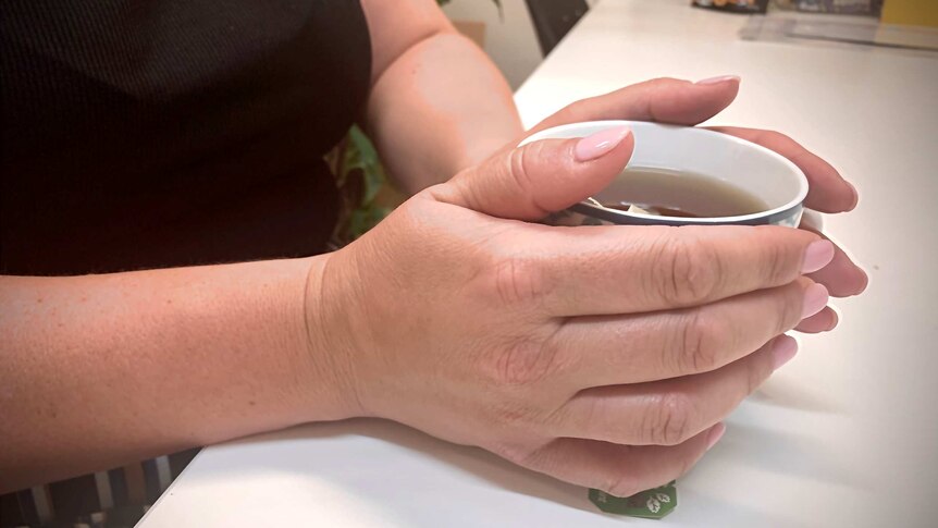 An undidentified woman holds a cup of tea with two hands.