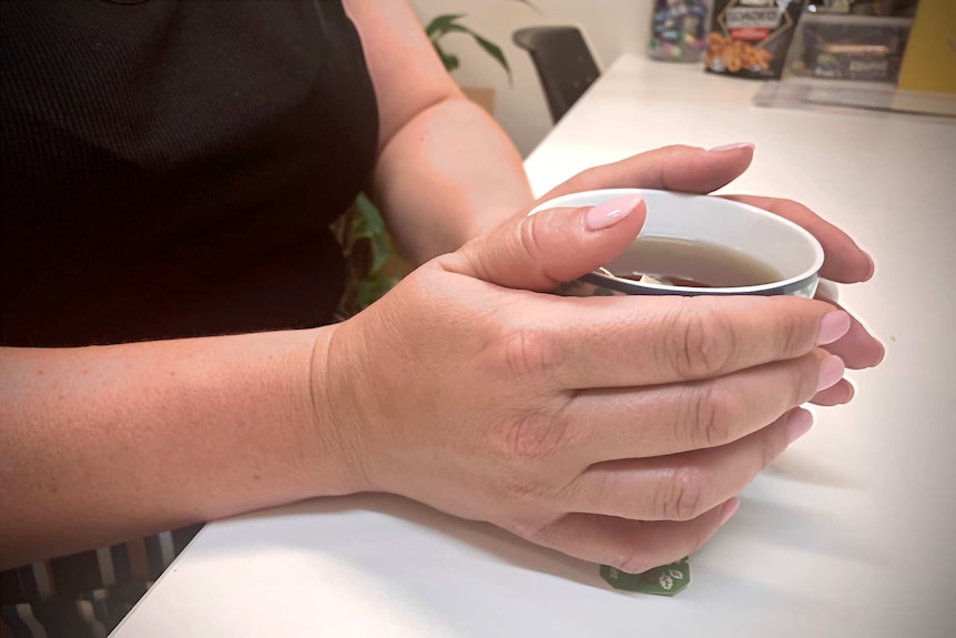 An undidentified woman holds a cup of tea with two hands.