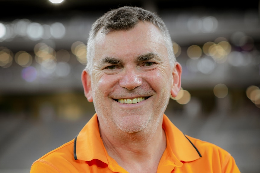 A man in an orange shirt smiles at the camera