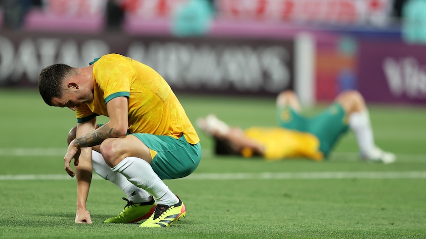 Football players lie on the ground looking devastated at a loss.