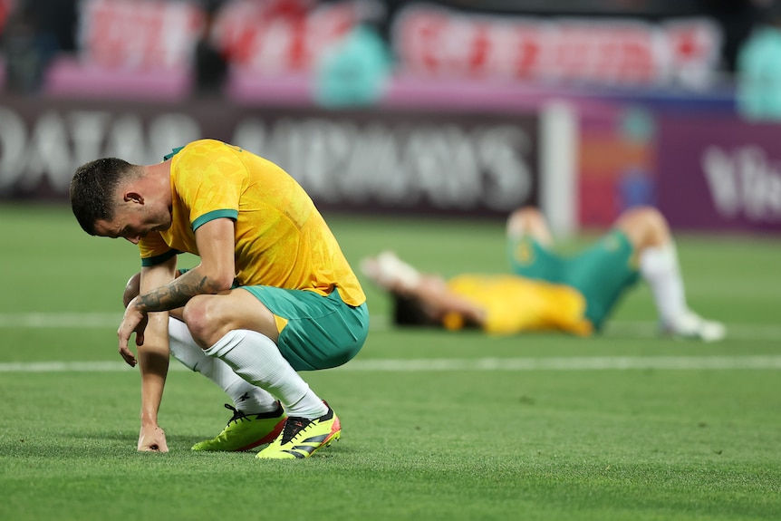 Football players lie on the ground looking devastated at a loss.