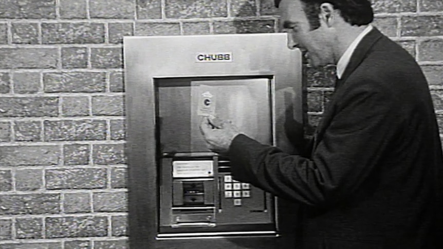 ABC reporter holds ATM card up at protoype machine in wall