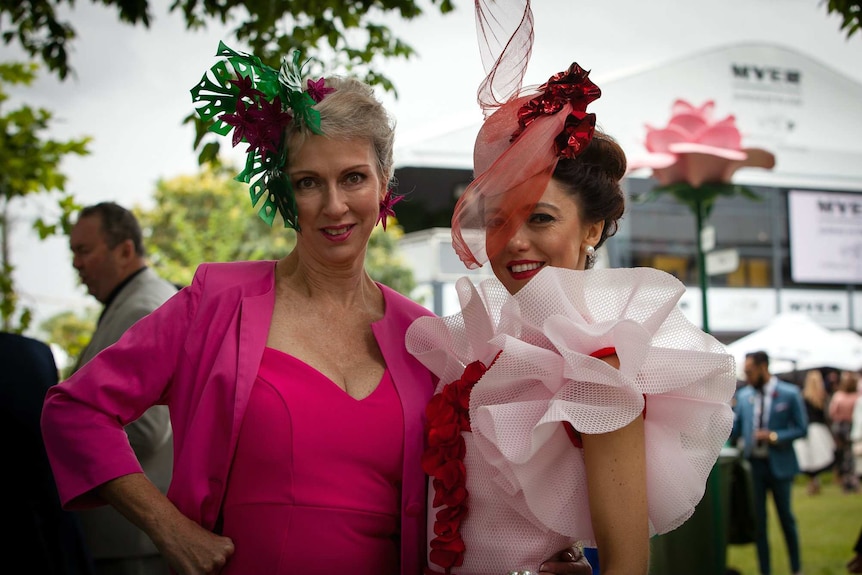 Two women wearing pink dresses pose at the Melbourne Cup