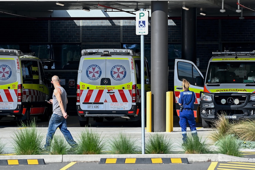 A man walks past a row of ambulances waiting outside a hospital. 
