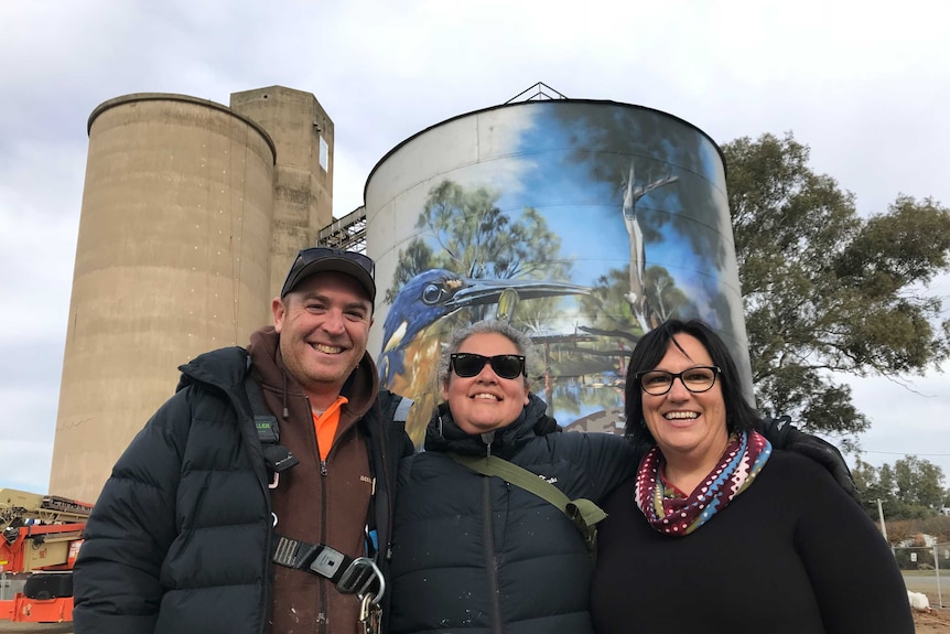 The artist Jimmy DVate stands with his wife, Carmen, and Rochester woman Kate Taylor. The mural towers behind them.