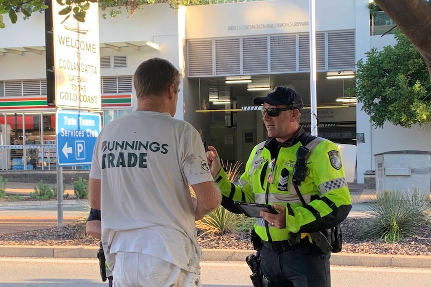 A police officer in high-vis speaks to a man wearing a Tshirt that says "Bunnings TRADE"