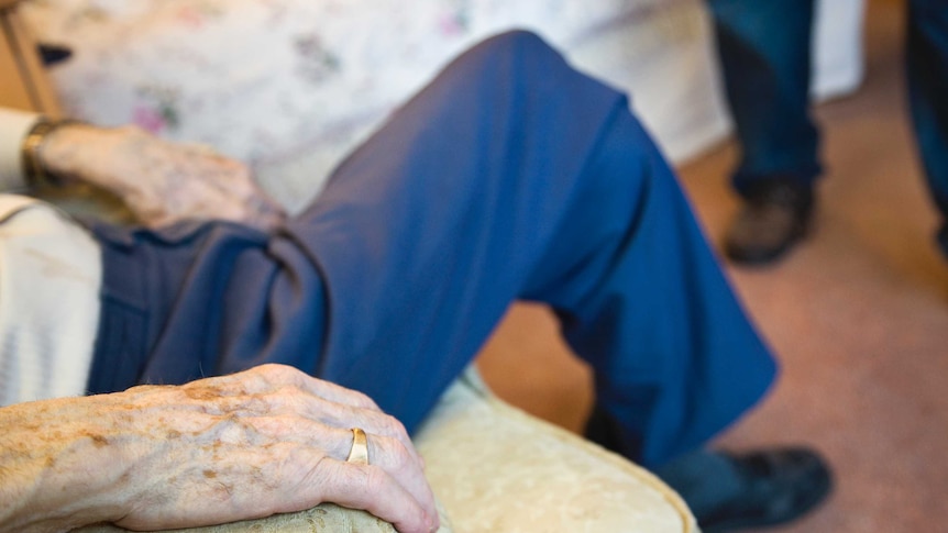 The hand of an elderly man sitting in an armchair in a nursing home.