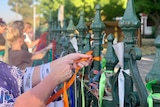 A close up of a woman's hands tying an orange ribbon to a cast iron fence