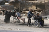 Two men in wheelchairs being pushed by a man and a woman.