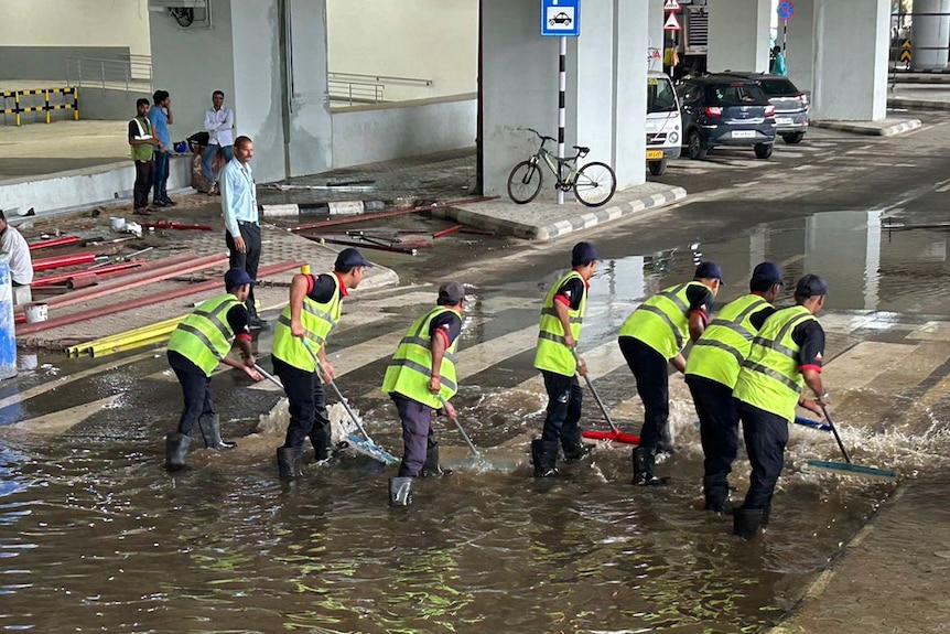 Men push water from a flooded water wearing fluro yellow vests.