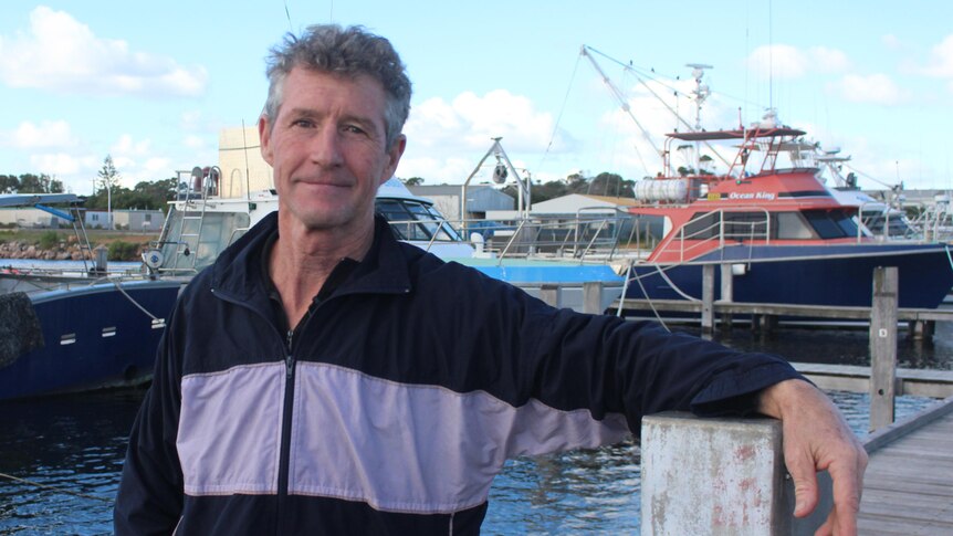 He stands at the Esperance boat harbour, with boats behind him